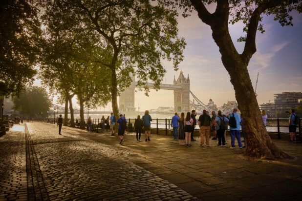 Dawn view of the Tower of London from the Queen's Walk along the Thames River with people standing around