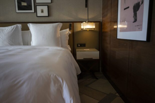 View of a hotel bed and nightstand, with artwork on the walls