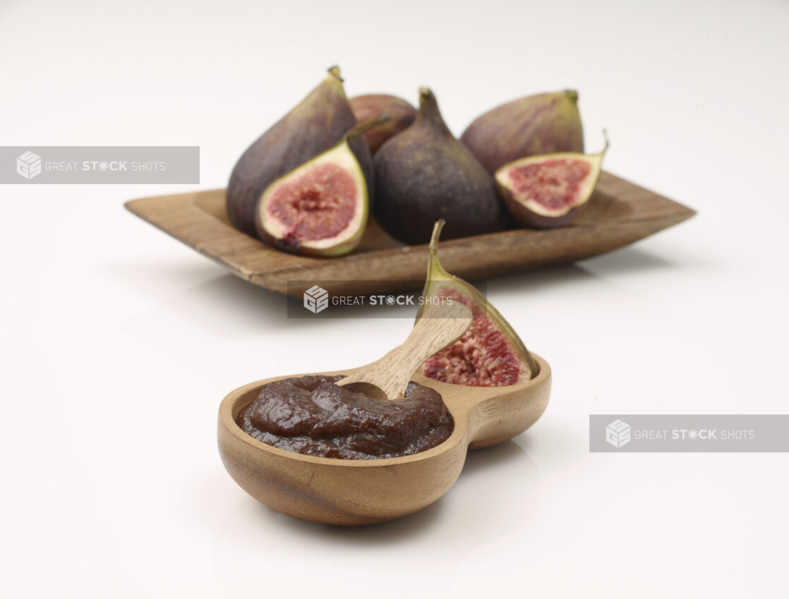 Wooden Bowl of Puréed Fig Sauce with a Wooden Spoon and Fresh Cut and Whole Figs in Background Isolated on a White Background