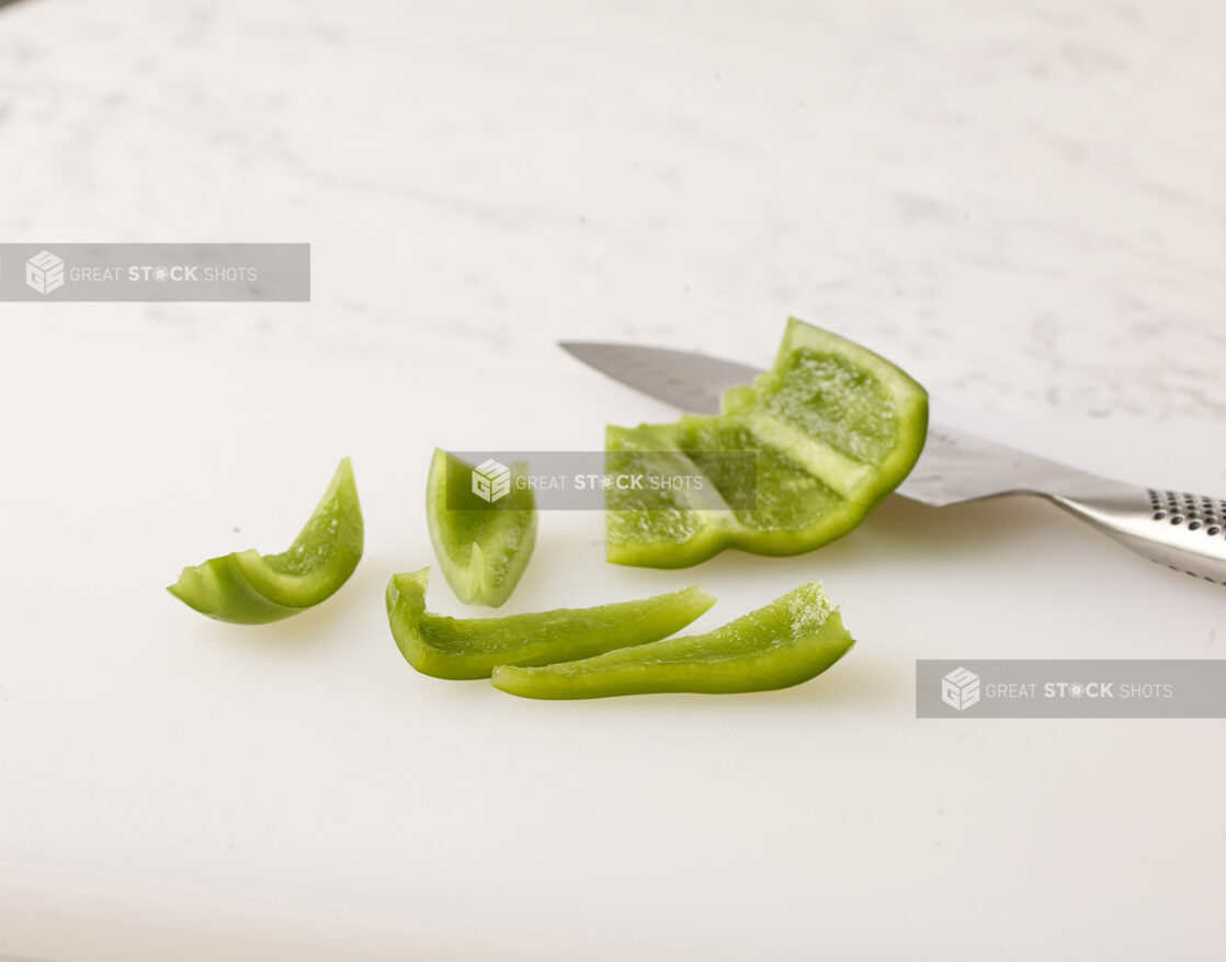 Green bell pepper sliced with a kitchen knife on a white cutting board