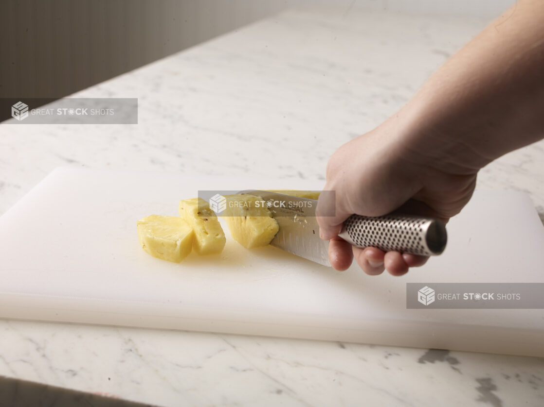 Hand cutting a cleaned pineapple on a white cutting board using a kitchen knife