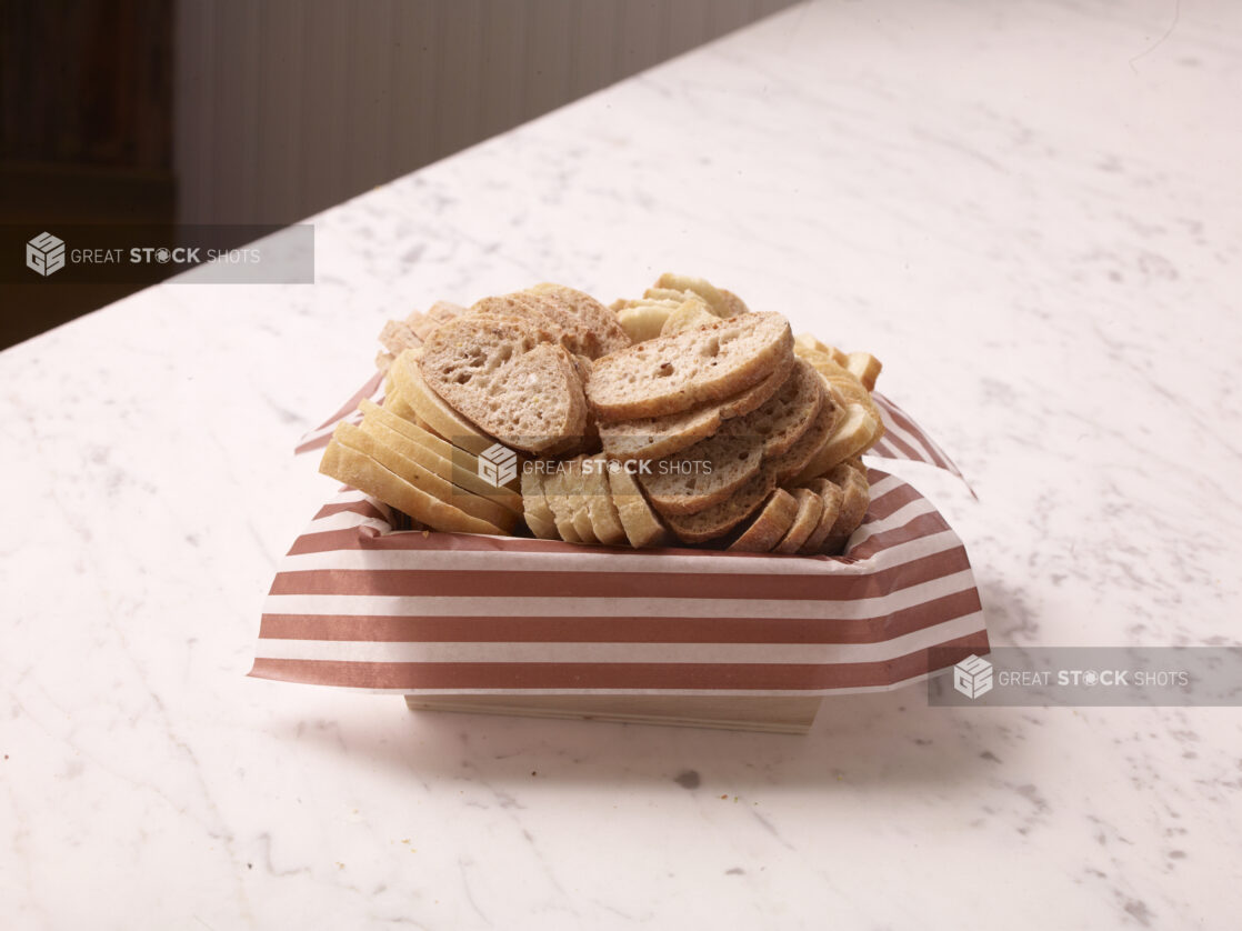 Wood catering tray lined with parchment paper with sliced baguettes on a marble countertop