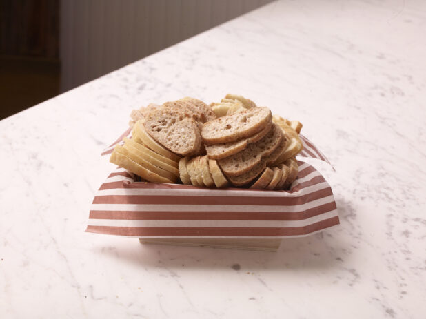 Wood catering tray lined with parchment paper with sliced baguettes on a marble countertop