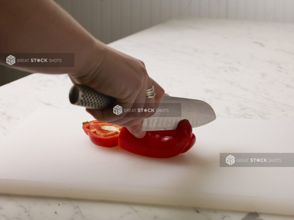 Woman cutting a red pepper on a white cutting board with a white marble background