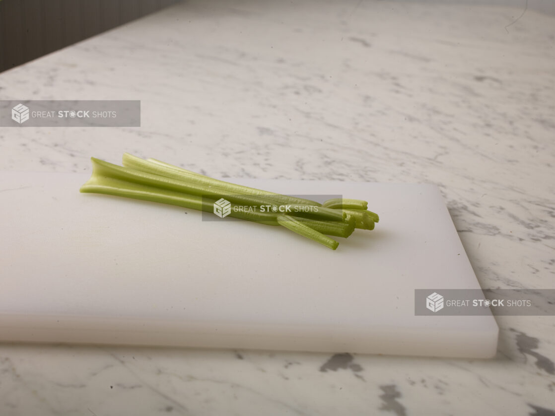 Two stalks of celery  on a white cutting board with a white marble background