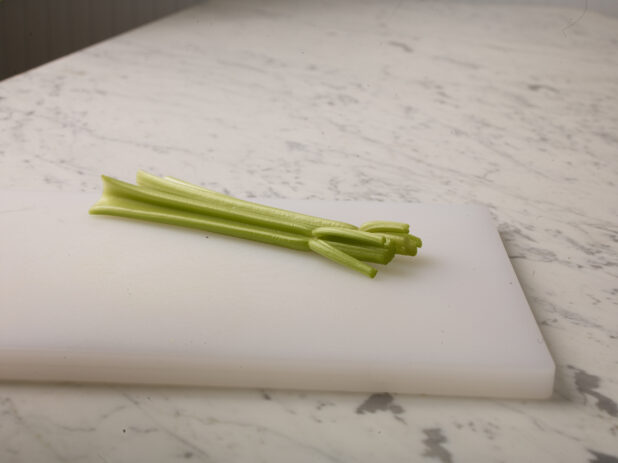 Two stalks of celery  on a white cutting board with a white marble background