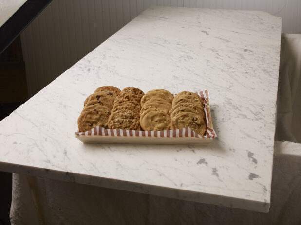 Wood catering tray of two dozen assorted cookies on a marble countertop