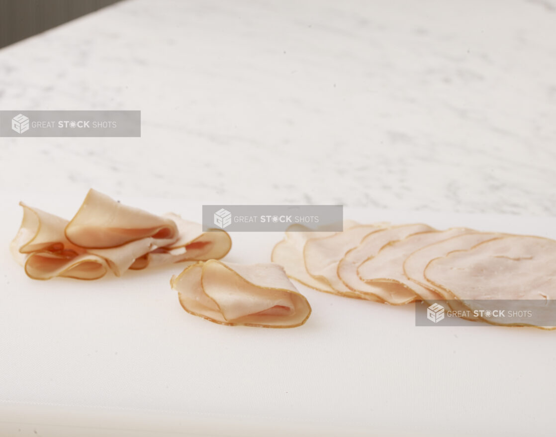 Thinly sliced over roasted turkey meat layered and folded on a cutting board on a white marble countertop