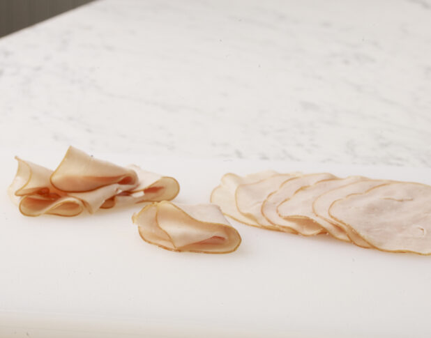 Thinly sliced over roasted turkey meat layered and folded on a cutting board on a white marble countertop