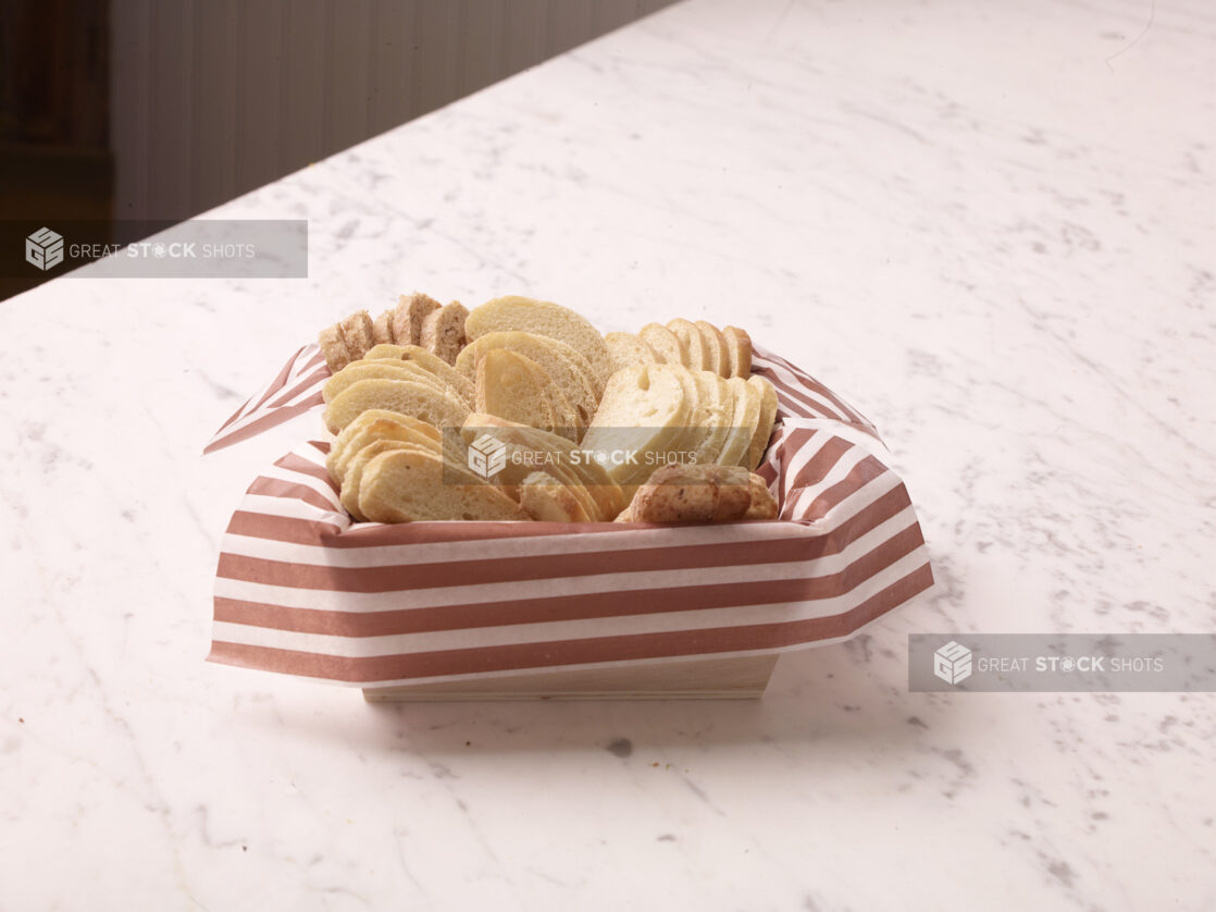 Wood catering tray lined with parchment paper with sliced baguettes on a marble countertop