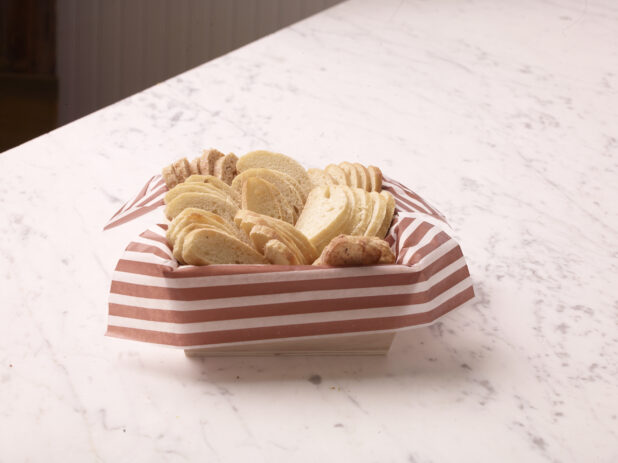 Wood catering tray lined with parchment paper with sliced baguettes on a marble countertop