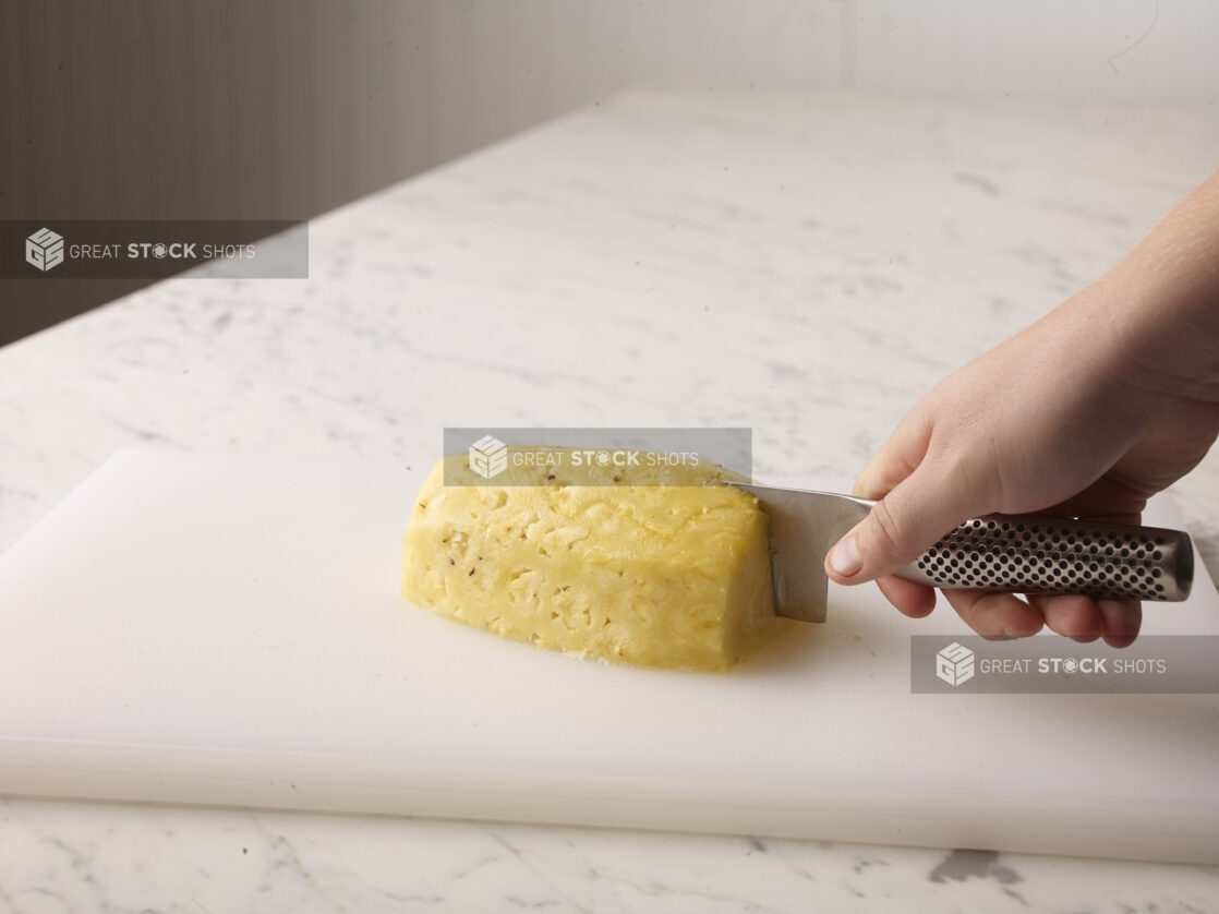 Hand cutting a cleaned pineapple on a white cutting board using a chefs knife (Global)