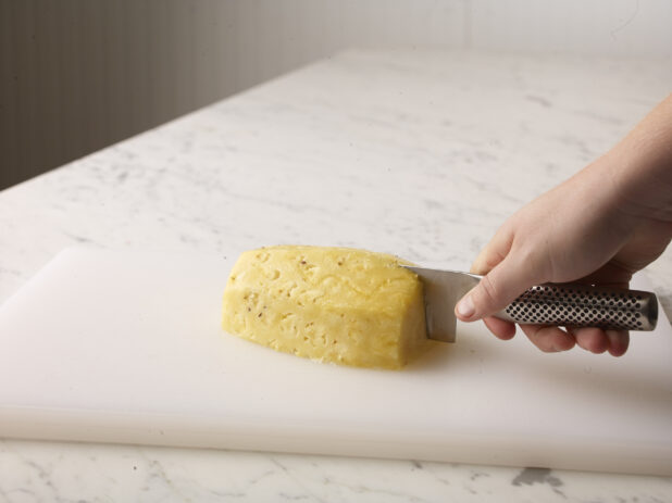 Hand cutting a cleaned pineapple on a white cutting board using a chefs knife (Global)