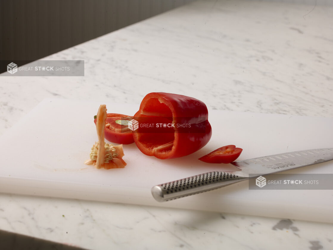 Cut red pepper with core removed on a white cutting board with a white marble background