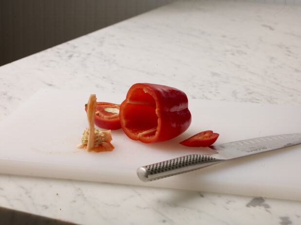 Cut red pepper with core removed on a white cutting board with a white marble background