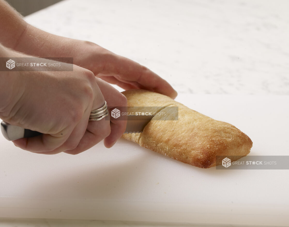 Woman cutting a white bun in half on a white cutting board with a white marble background