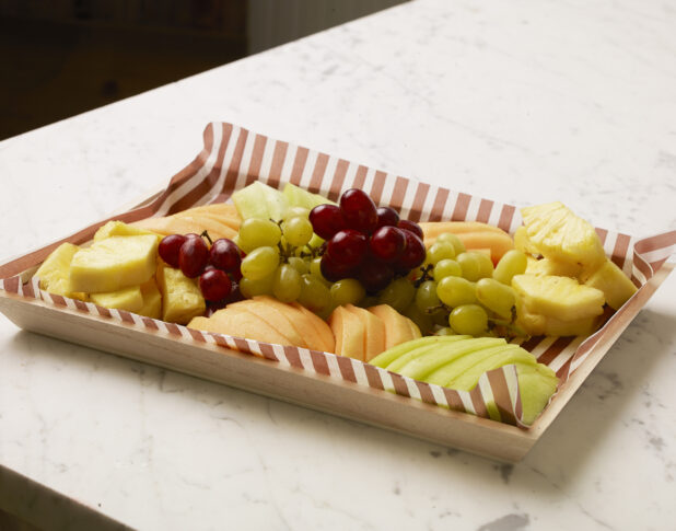 Wood catering tray of assorted fruit on a marble countertop