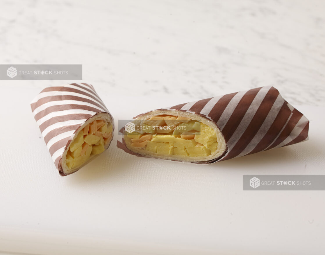 Egg and cheddar cheese breakfast wrap, wrapped in brown and white striped wrapping paper on a white background