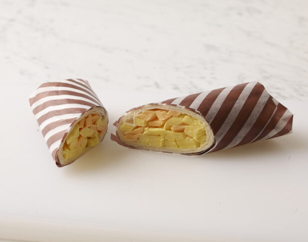Egg and cheddar cheese breakfast wrap, wrapped in brown and white striped wrapping paper on a white background