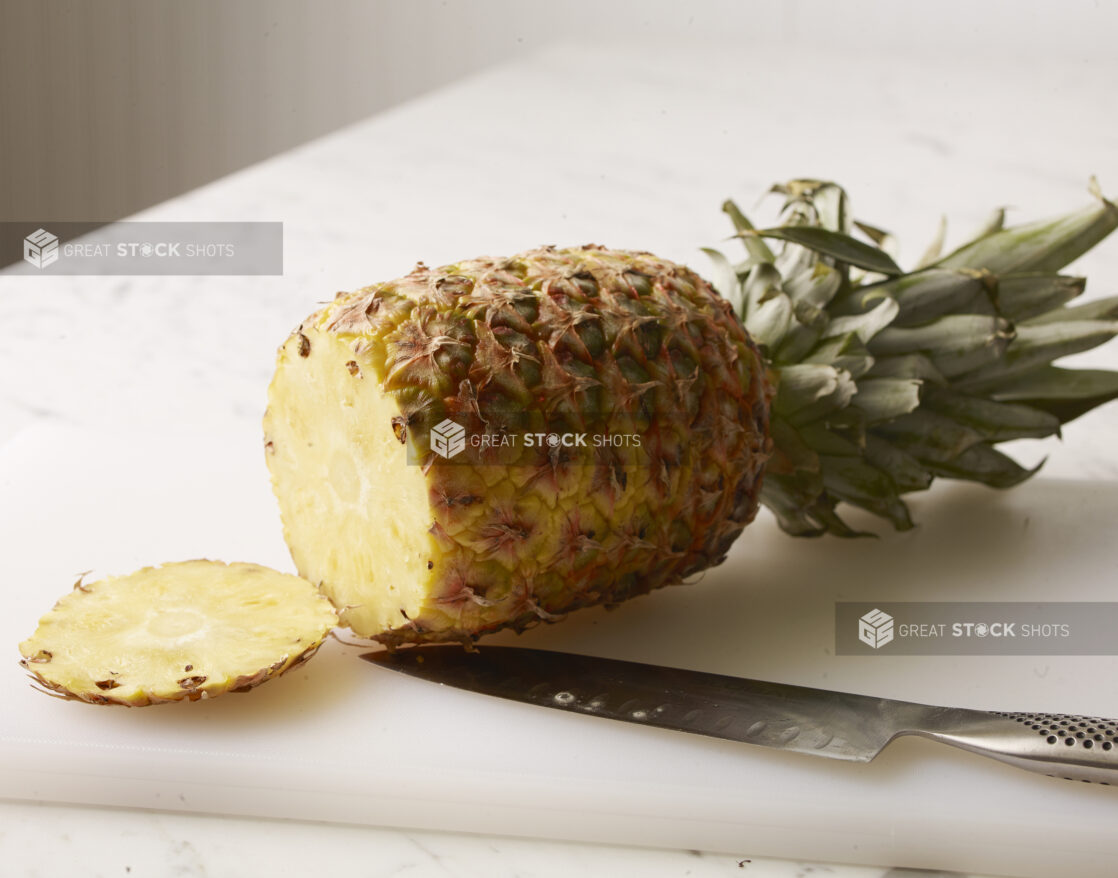 Whole pineapple with bottom end cut off on a white cutting board with a chefs knife on the board