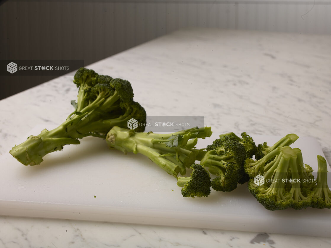 Chopped fresh broccoli on a white cutting board with a white marble background