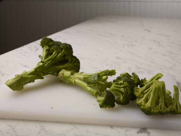 Chopped fresh broccoli on a white cutting board with a white marble background