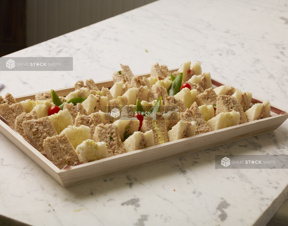 Tuna and Egg Salad Crustless Finger Sandwiches on Whole Wheat and White Bread on a Wooden Serving Tray for Catering, on a White Marble Counter Top in a Kitchen Setting