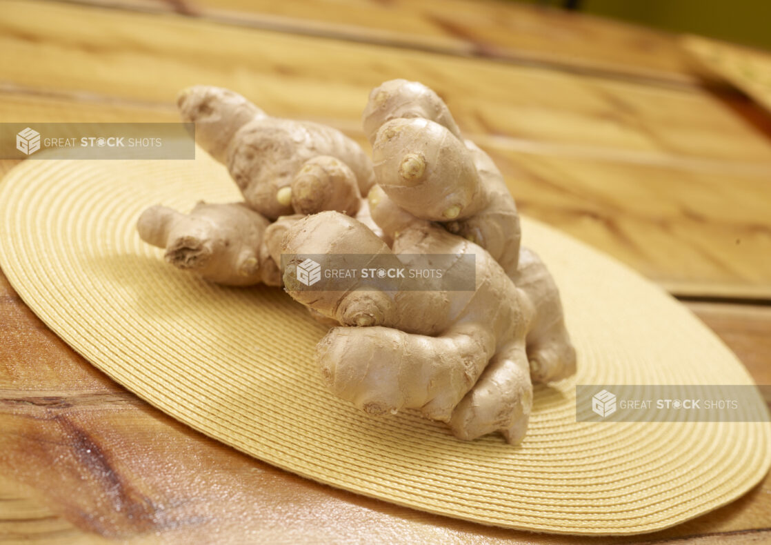 Close Up of a Pile of Ginger Roots on a Yellow Placemat on a Wooden Table in an Indoor Setting