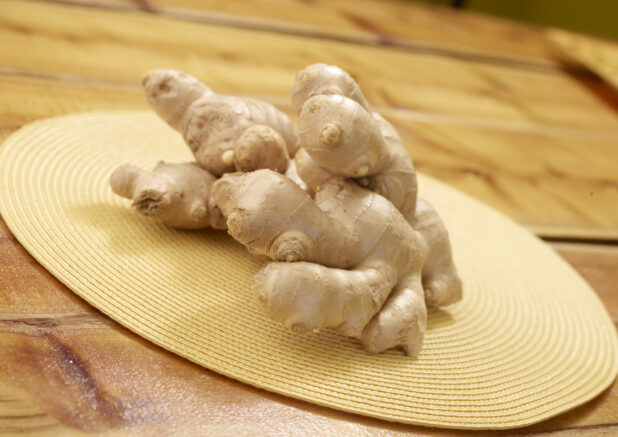 Close Up of a Pile of Ginger Roots on a Yellow Placemat on a Wooden Table in an Indoor Setting