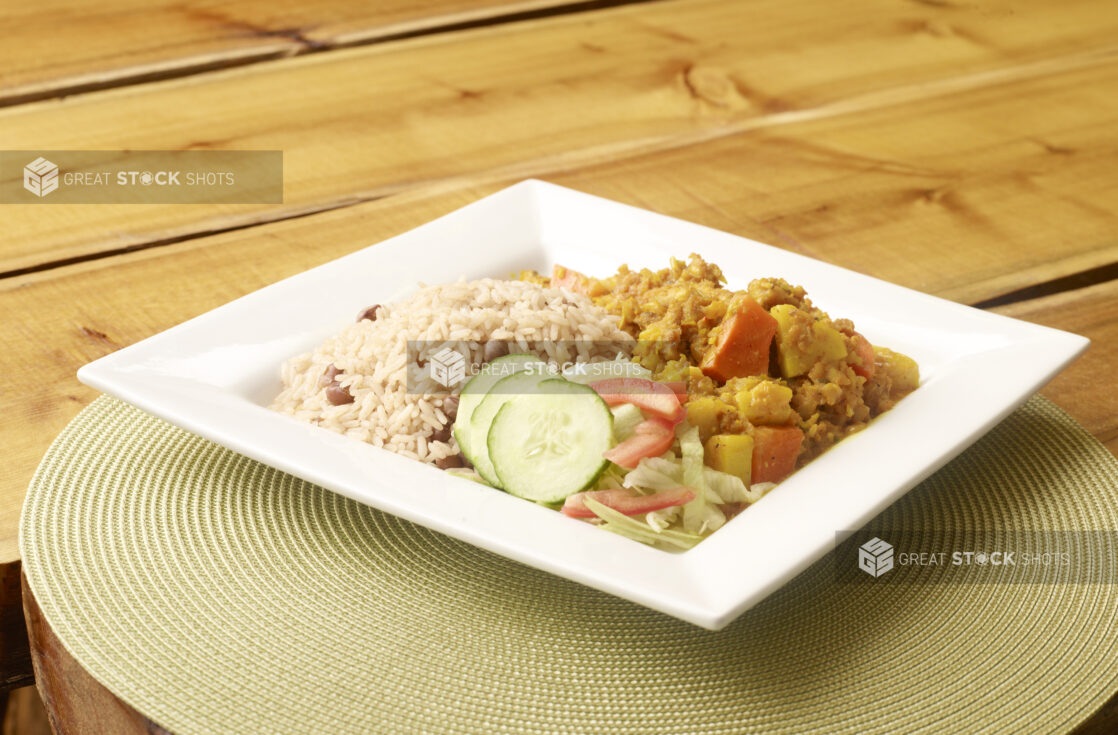 Curried Ackee and Salt Fish Dinner Platter with Red Beans and Rice and Salad on White Square Plate on Wooden Table with Bokeh Effect