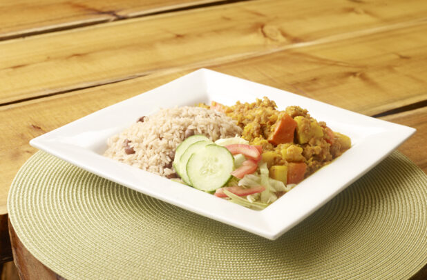 Curried Ackee and Salt Fish Dinner Platter with Red Beans and Rice and Salad on White Square Plate on Wooden Table with Bokeh Effect