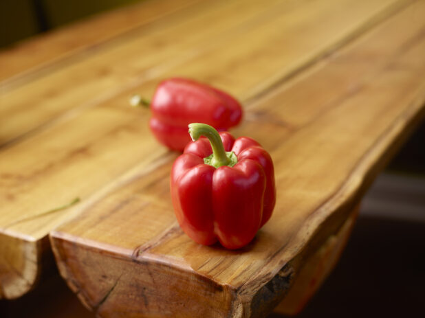 Fresh Whole Red Bell Peppers on Wooden Table with Bokeh Effect