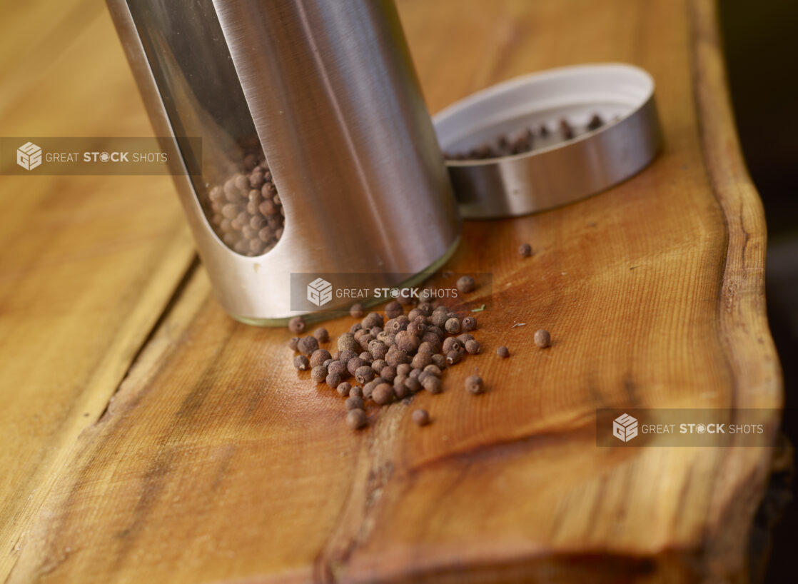 Whole Dried Allspice Peppercorns with Stainless Steel Pepper Mill on Wooden Table with Bokeh Effect