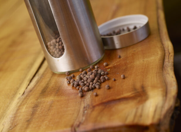Whole Dried Allspice Peppercorns with Stainless Steel Pepper Mill on Wooden Table with Bokeh Effect