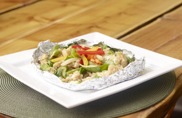 Salt Fish, Okra and Peppers Cooked in Tin Foil on a Square White Dish on a Wooden Table with Bokeh Effect
