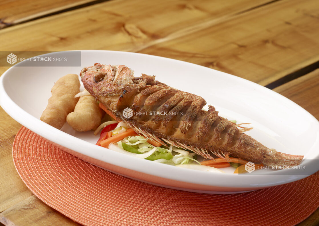 Large White Platter of Whole Oven Roasted Red Snapper with Vegetables and Fried Bread on Wooden Table