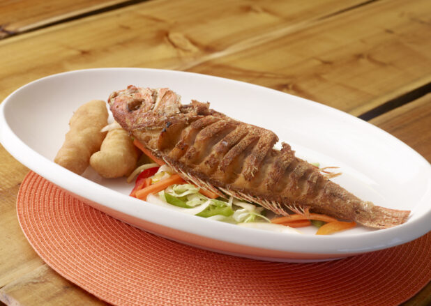 Large White Platter of Whole Oven Roasted Red Snapper with Vegetables and Fried Bread on Wooden Table