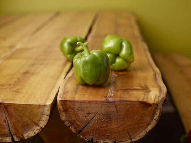 Fresh Whole Green Bell Peppers on Wooden Table with Bokeh Effect