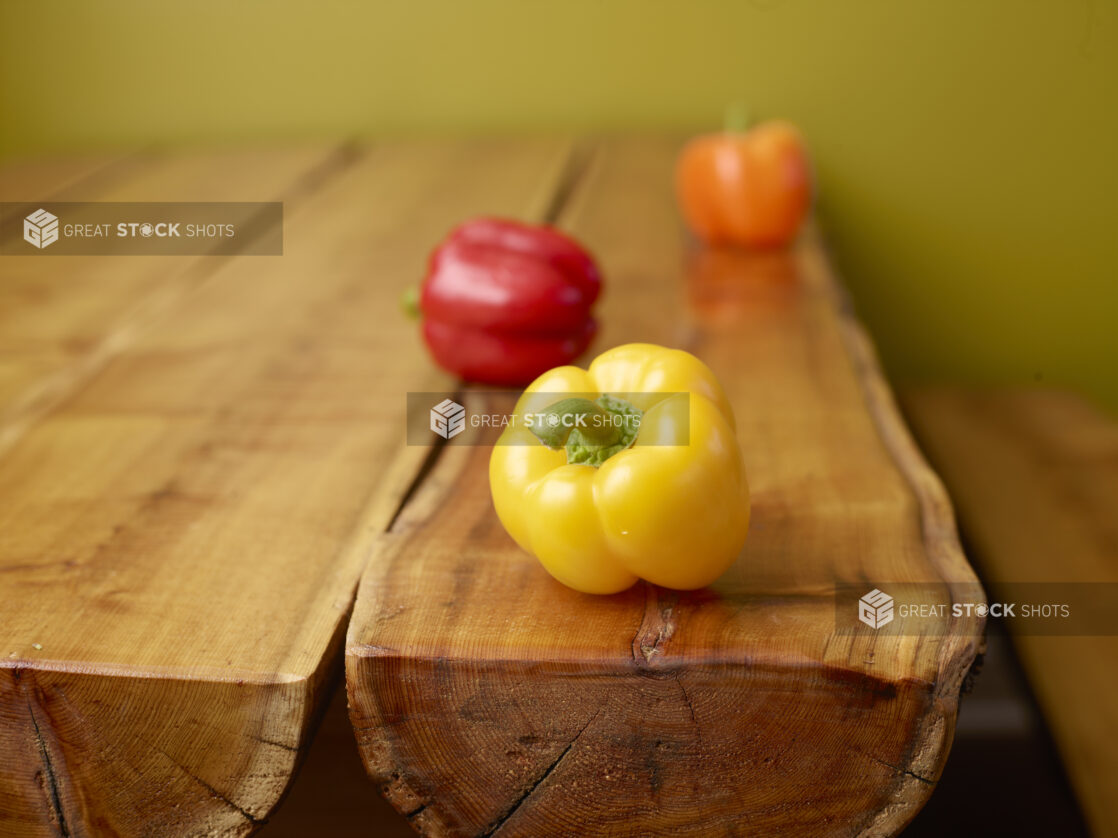 Whole Yellow, Red and Orange Bell Peppers on a Wooden Table with Green Background and Bokeh Effect