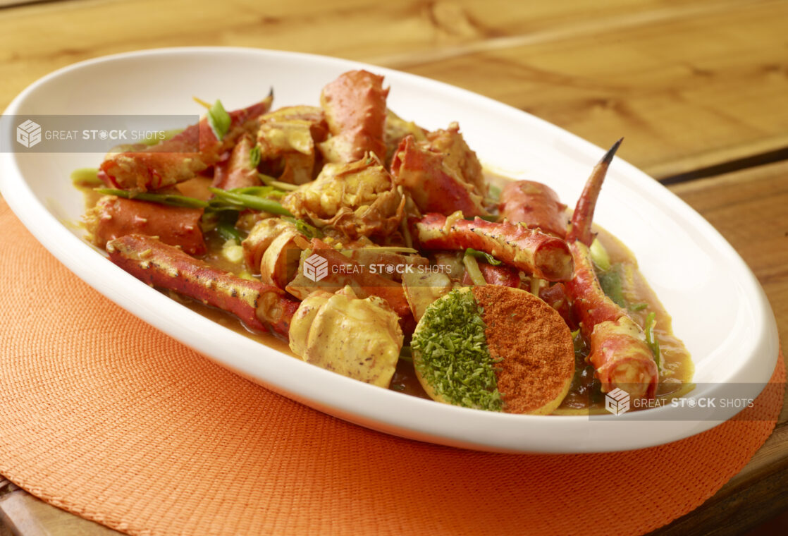 Caribbean King Crab Stew with Cracker on Large White Platter on Wooden Table with Bokeh Effect