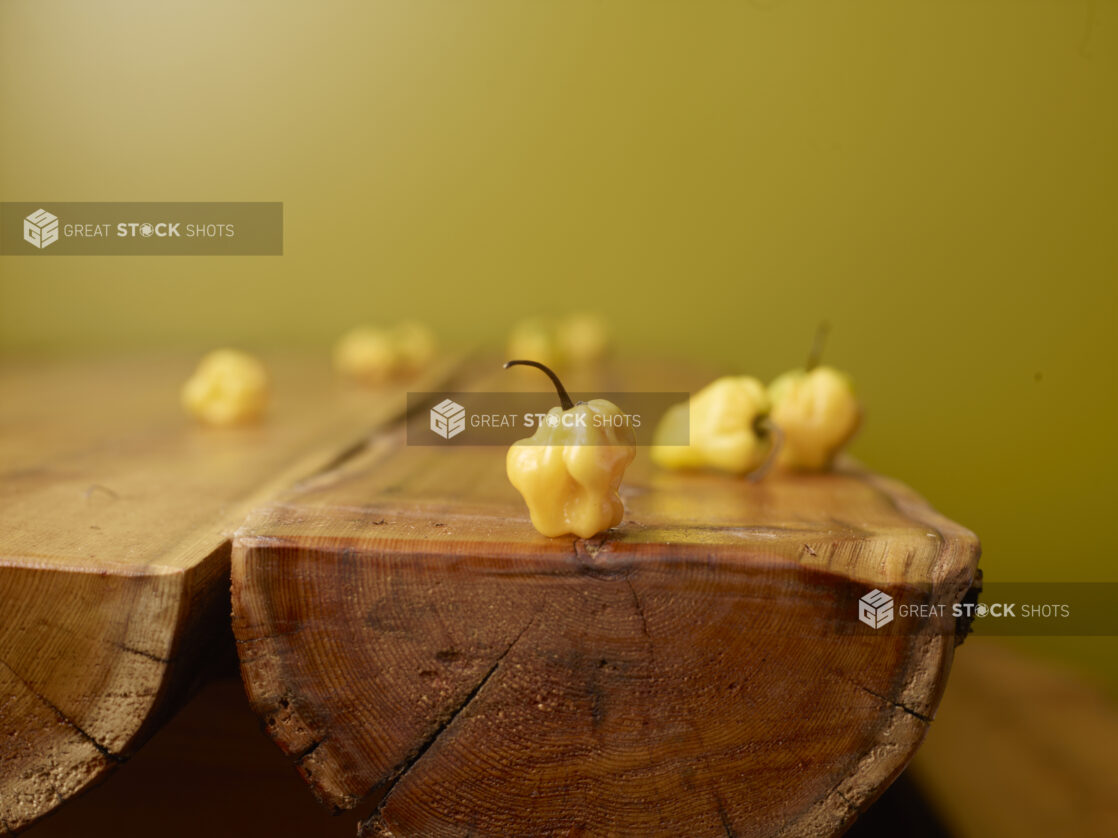 Whole Raw Yellow Scotch Bonnet Peppers on Wooden Table with Green Background and Bokeh Effect