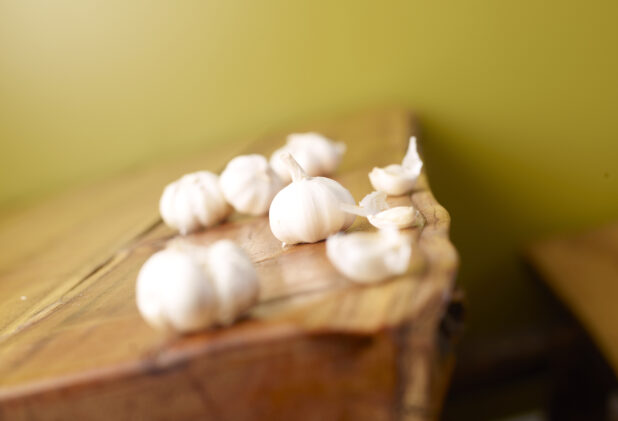 Raw, Unpeeled Cloves of Garlic on Wooden Table with Green Background and Bokeh Effect