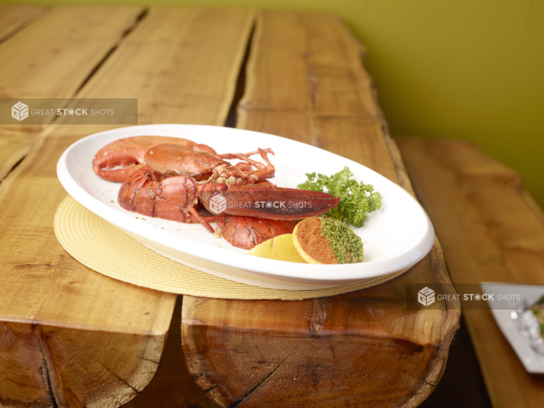 Whole Boiled Lobster Cut into Quarters on a Large White Platter with a Lemon Wedge and Cracker on a Wooden Table