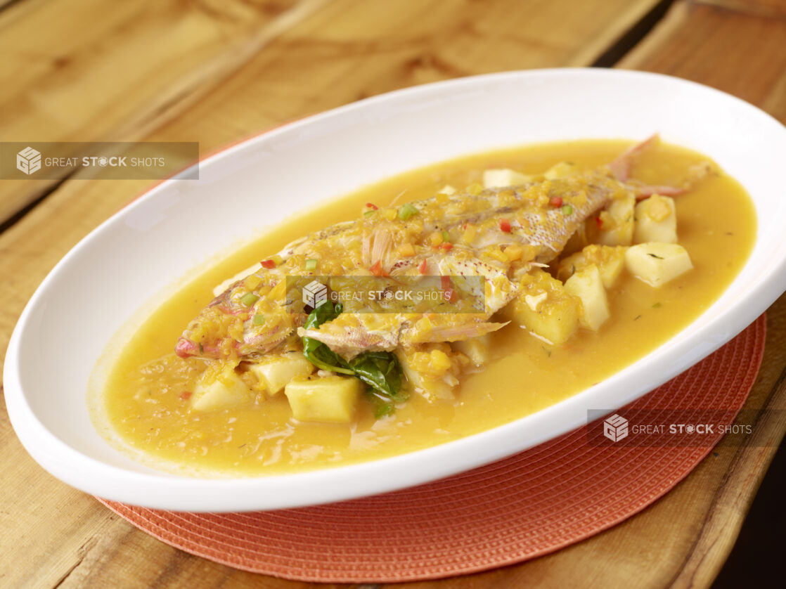 Whole Red Snapper Stew with Potatoes in a Large White Platter on an Orange Placemat on a Wooden Table - Variation