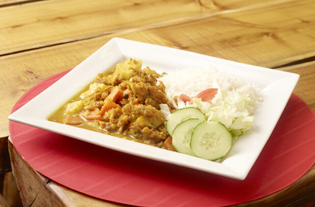 Jamaican Curried Fish Stew on White Square Plate with White Rice and Salad on a Red Placemat on a Wooden Table