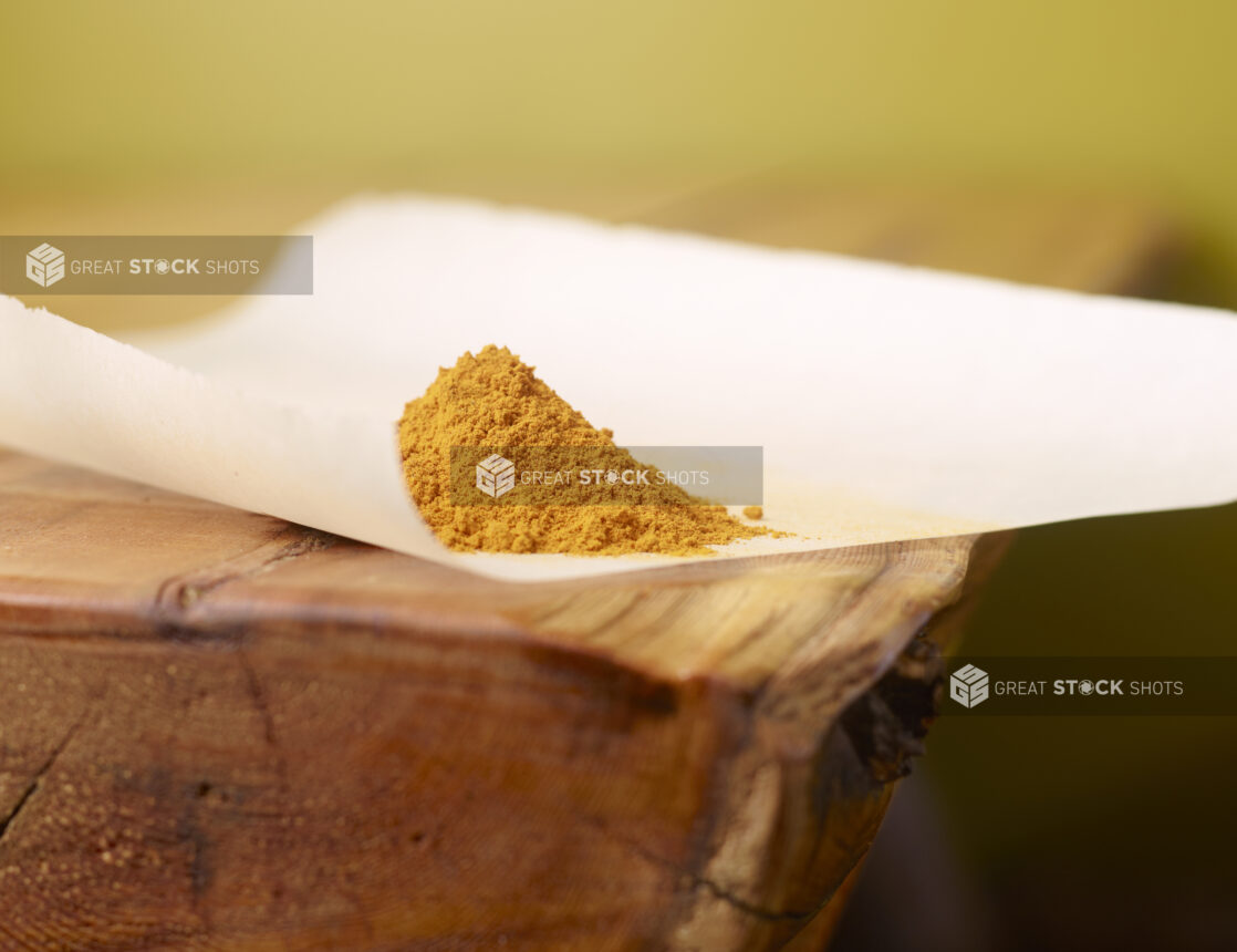 Close Up of Turmeric Powder Piled on Top of White Parchment Paper on a Wooden Table with Bokeh Effect