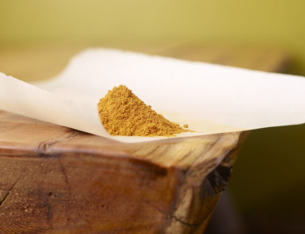 Close Up of Turmeric Powder Piled on Top of White Parchment Paper on a Wooden Table with Bokeh Effect