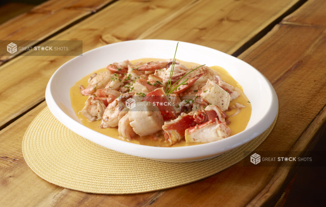 Seafood Stew with Crab Legs, Scallops and Shrimp and Chive Garnish on a Yellow Placemat on a Wooden Table