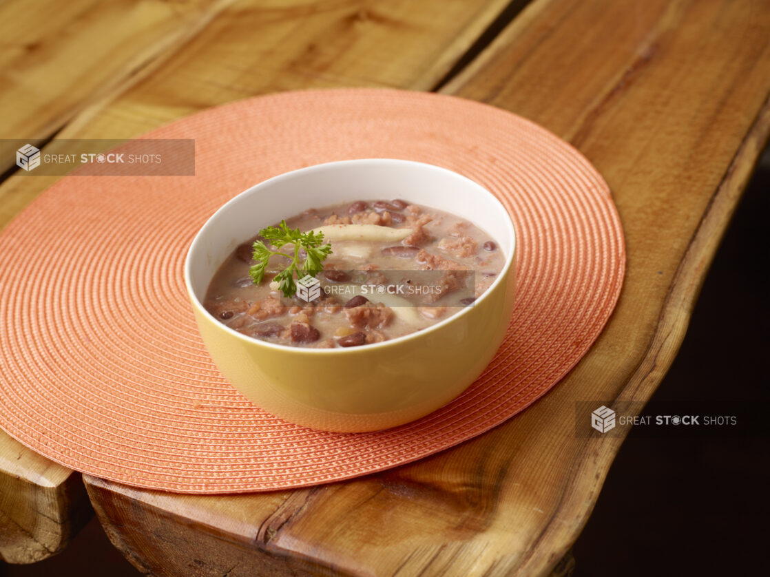 Jamaican Red Pea Soup with Jamaican Spinner Dumplings in a Yellow Ceramic Bowl on an Orange Placemat on a Wooden Table