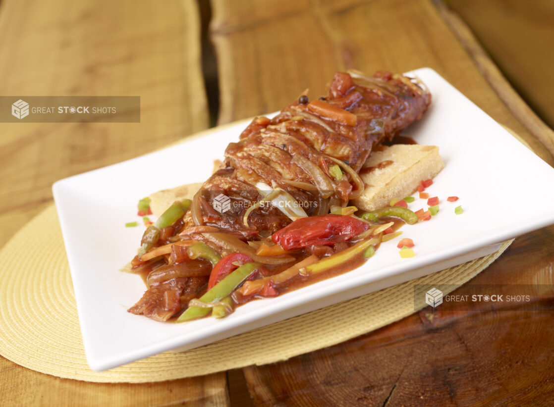 Caribbean Stewed Red Snapper Fish Platter with Creole Sauce, Vegetables on a Square White Platter on a Wooden Table